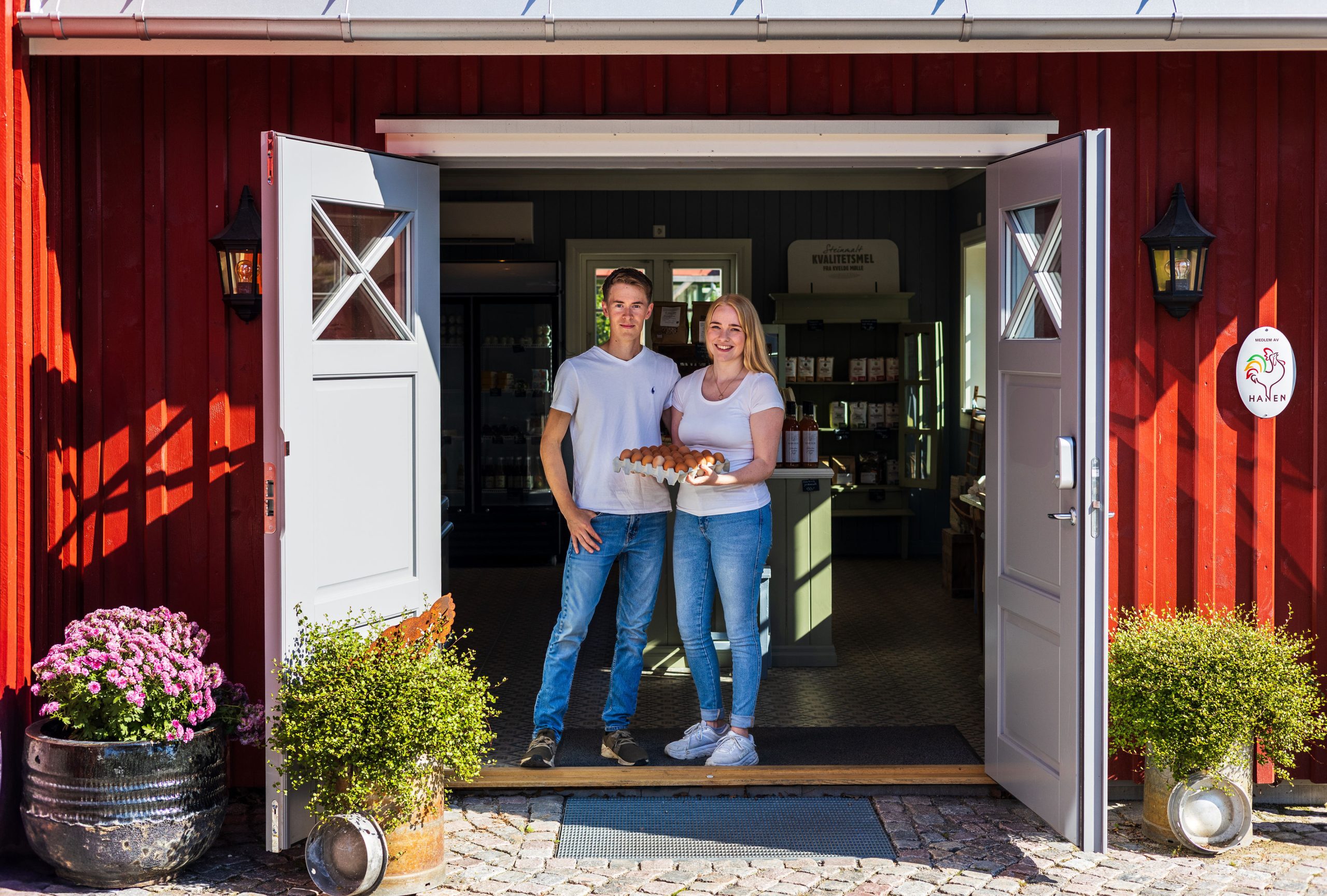 To personer fra Møyland Gårdsbutikk står i døråpningen til gårdsbutikken og holder et brett med egg.