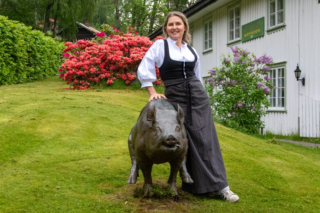 Solveig Barstad står ved en grisefigur foran Nutheim Gjestgiveri i Flatdal.