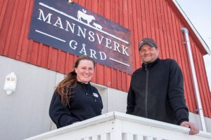 Driverne ved Mannsverk gård står foran den røde gårdsbygningen med skiltet «Mannsverk gård».