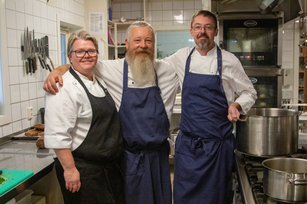 Tre kokker i arbeidsantrekk står sammen på kjøkkenet på Kringler Gjestegård.