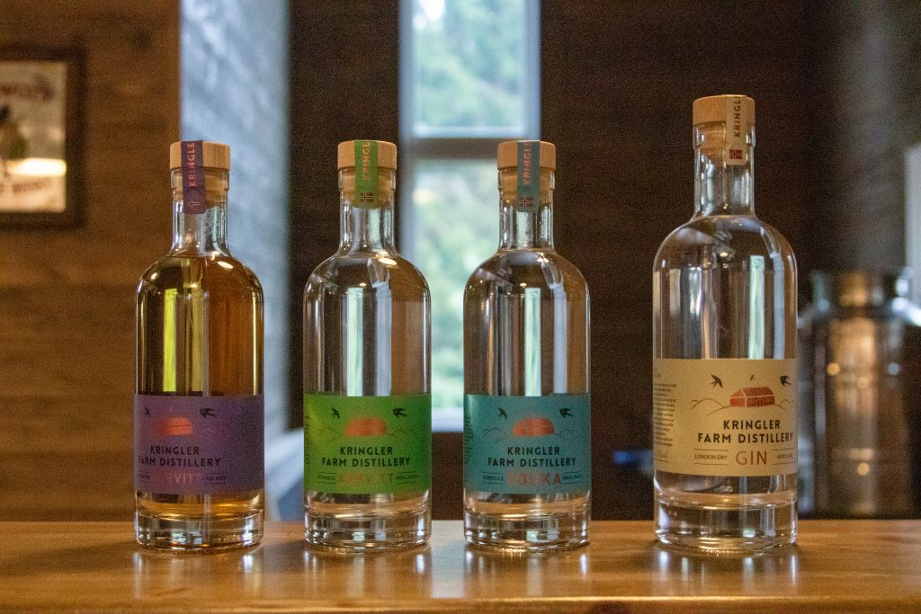 Fire flasker med akevitt, vodka og gin fra Kringler Gårdsdestilleri på en trebenk.