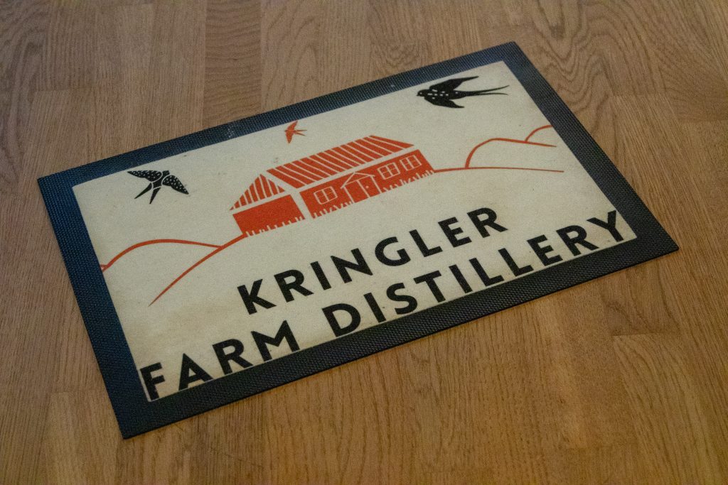 Matte med teksten «Kringler Farm Distillery» og illustrasjon av en rød gårdsbygning.