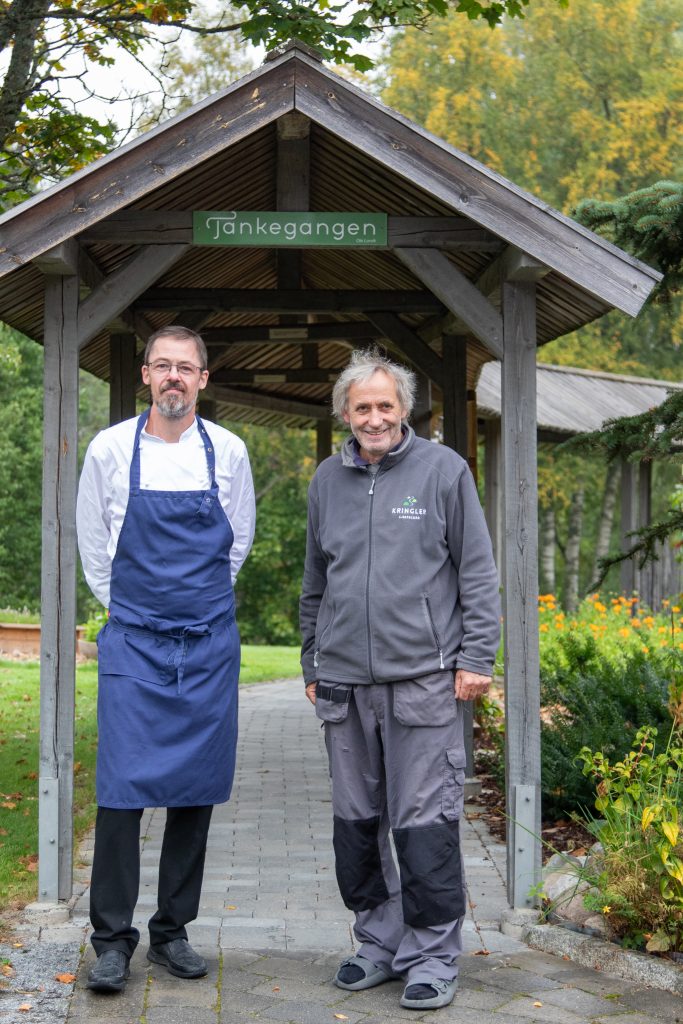 En kokk og en bonde står under den overbygde «Tankegangen» på Kringler Gjestegård.