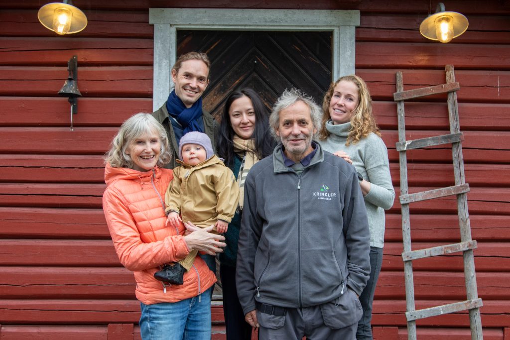 Gruppeportrett av fem voksne og et barn foran en rød trebygning på Kringler Gjestegård.