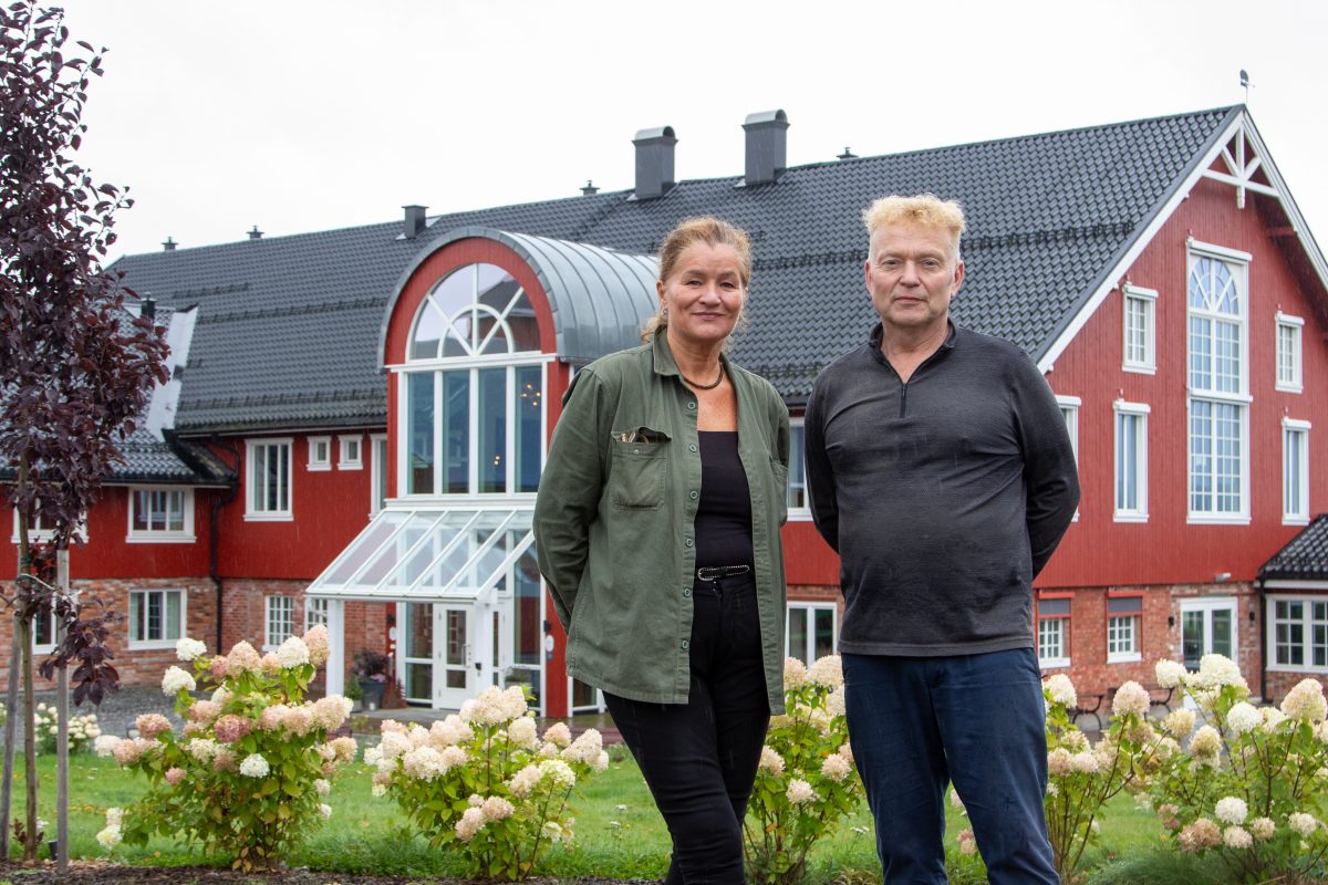 Randi Roggenbihl og en mann i samtale foran den røde bygningen til Smakfulle Rom på Asak gård.