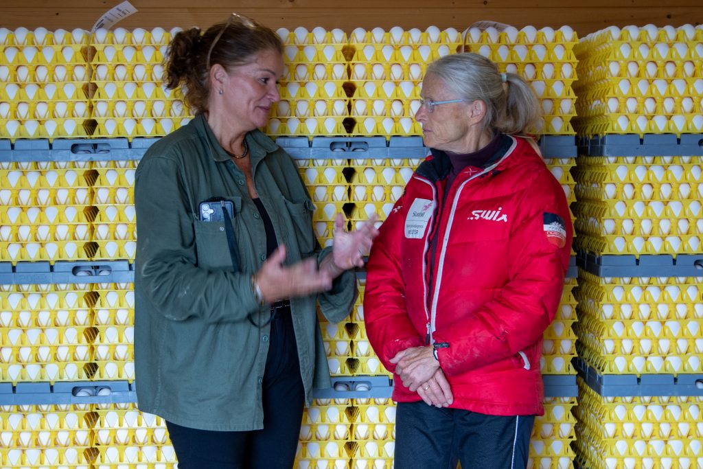 Randi Roggenbihl og eggprodusent Unni Weydahl i samtale foran stabler med eggbrett på Størsrud gård.
